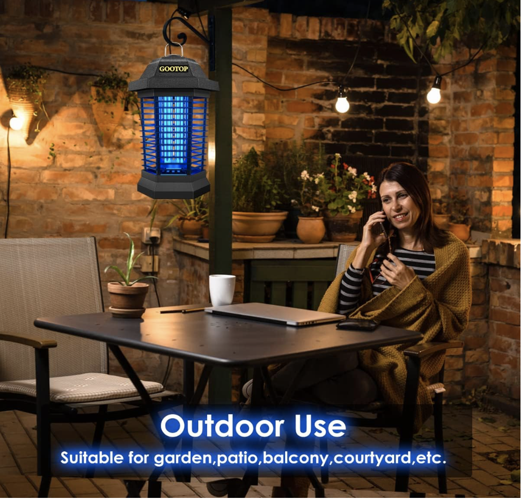 GOOTOP Bug Zapper hanging on a patio at night, glowing blue near a woman relaxing outdoors