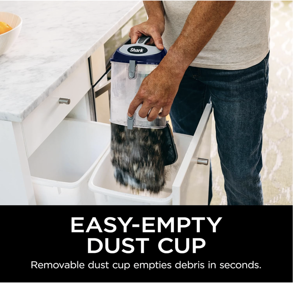 Close-up of the Shark NV360 vacuum’s removable dust cup being emptied into a trash bin, showing its simple bagless design.