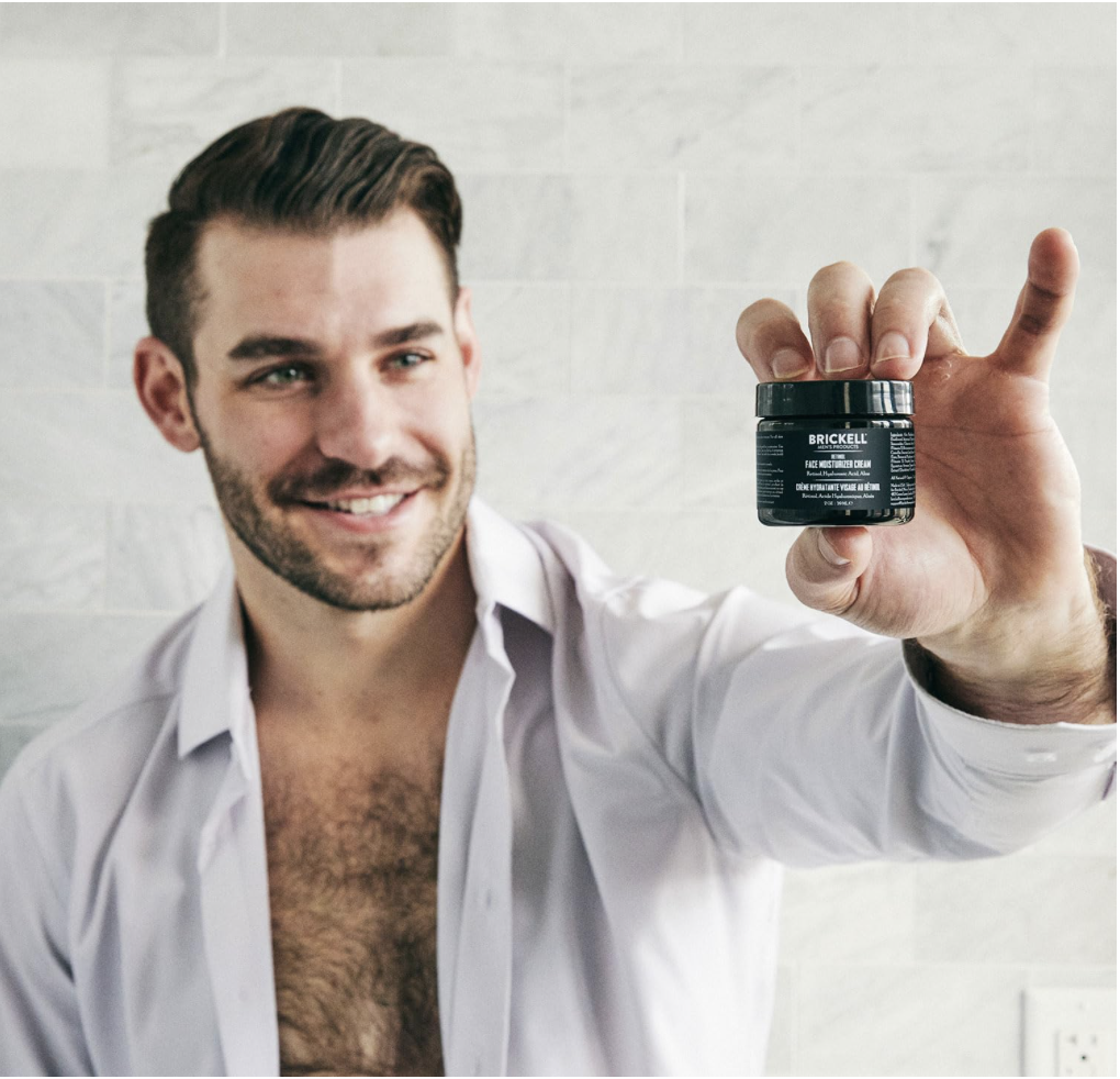 Smiling man holding Brickell Men’s Retinol Face Moisturizer Cream jar in hand.