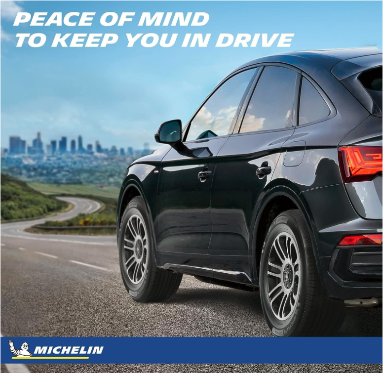 Crossover driving along a curved highway with Michelin Defender2 tires and city skyline in background